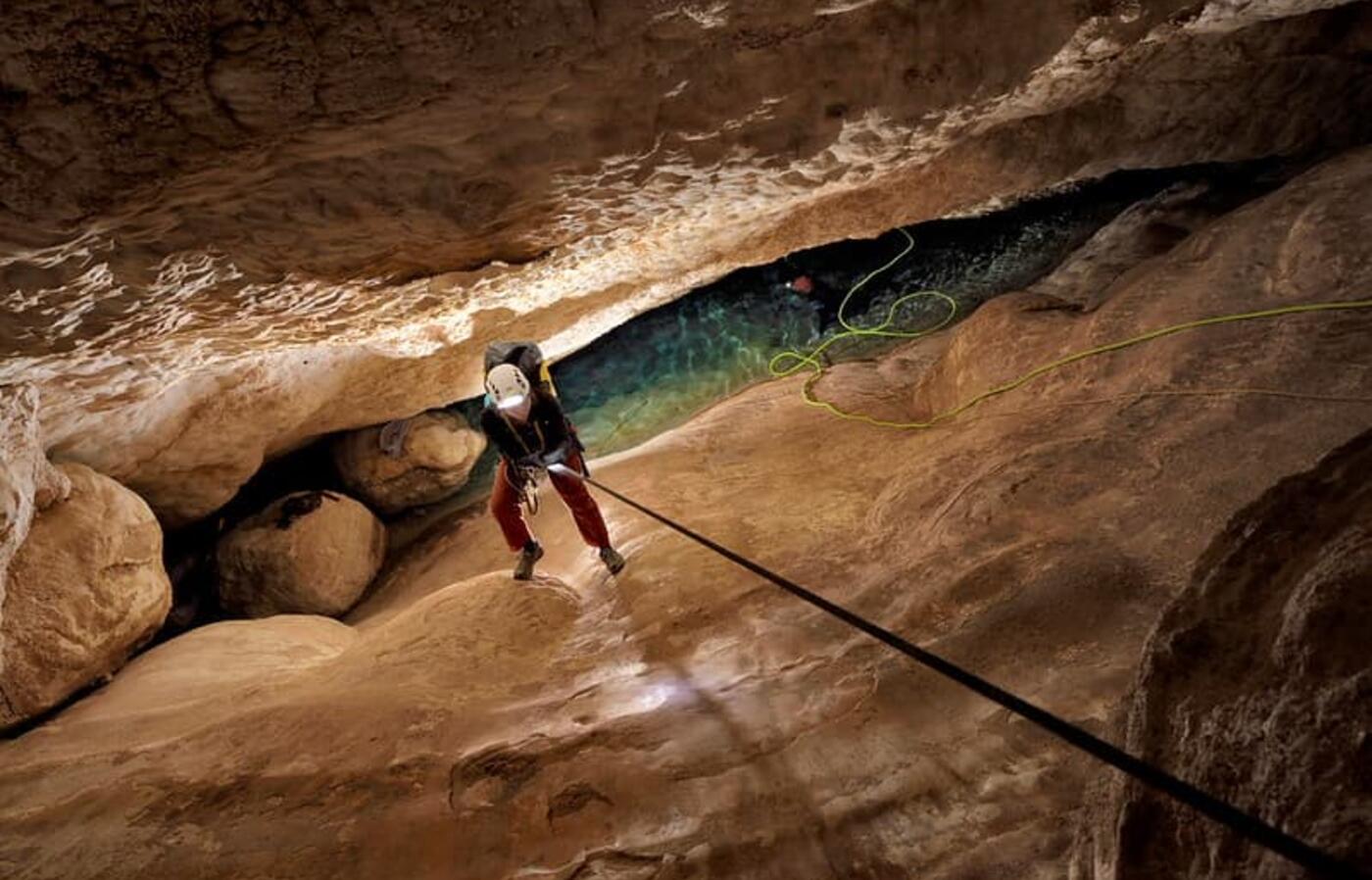 person climbing down a rope into a cave