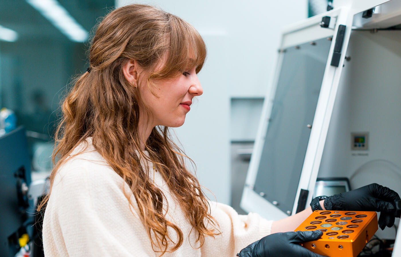 Woman in white lab coat handles samples under hood in lab.