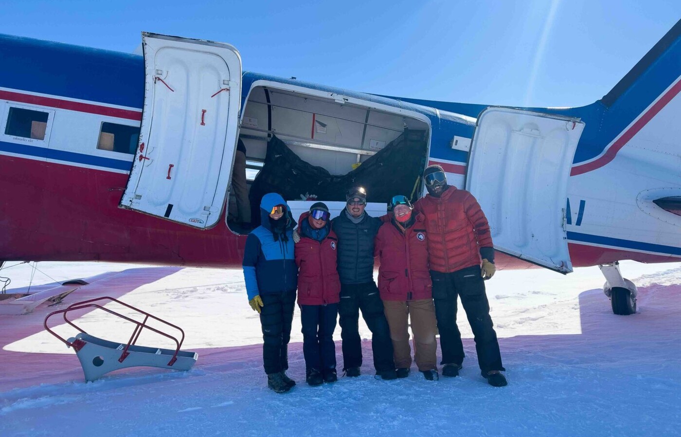 scientists standing in front of a plane on the snow