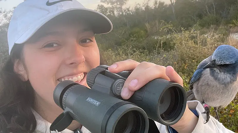 woman with binoculars and a bird sitting on her arm