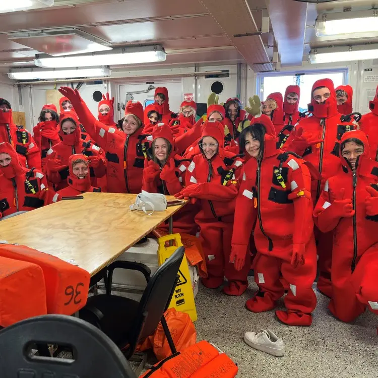 Students pose with "gumby suits" on a research vessel.
