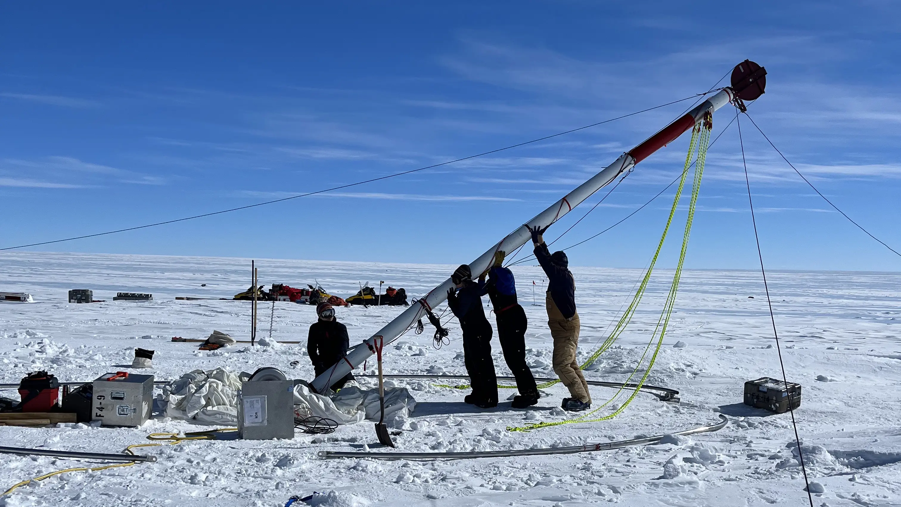 Four scientists work together to set up drilling tent in snowy Antarctic landscape.
