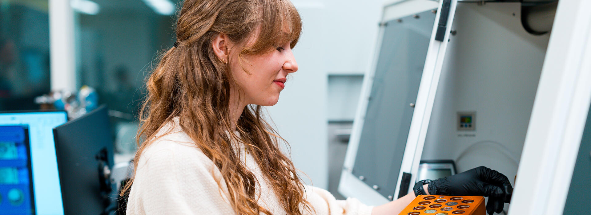 Woman in white lab coat handles samples under hood in lab.
