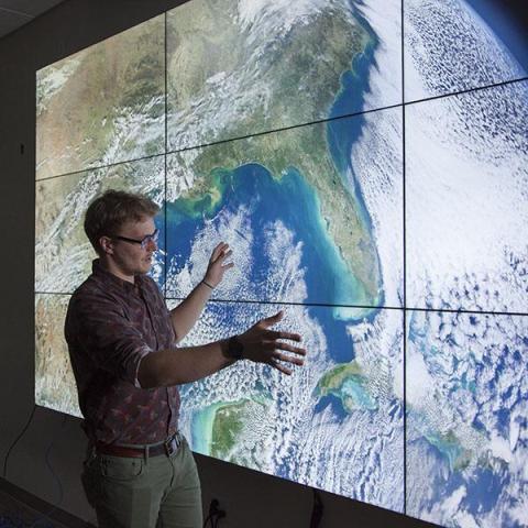 person at a screen with a satellite image covering a whole wall