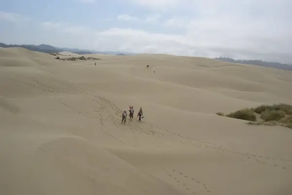 people in the distance walking across sand dunes