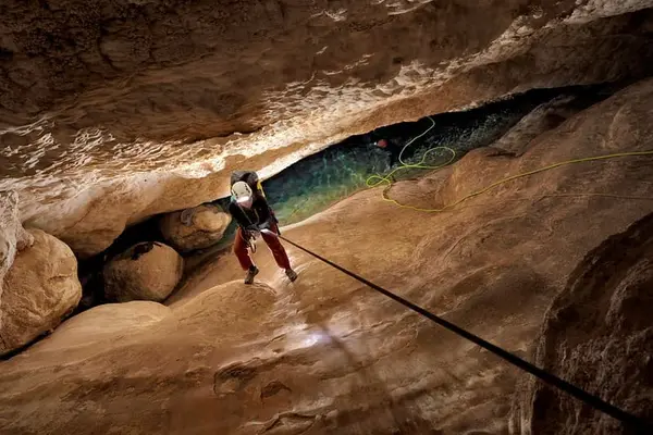 person climbing down a rope into a cave